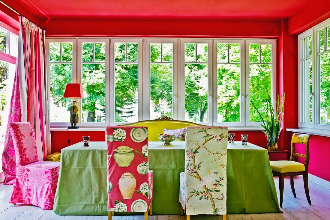 Farbenfroher Esszimmer-Anbau mit bunten, gemusterten Hussen und grüner Tischdecke, kombiniert mit rot getönten Wänden