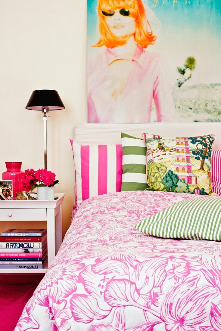 Large portrait of woman, scatter cushions with broad stripes and white and pink bed linen with large floral pattern in bedroom