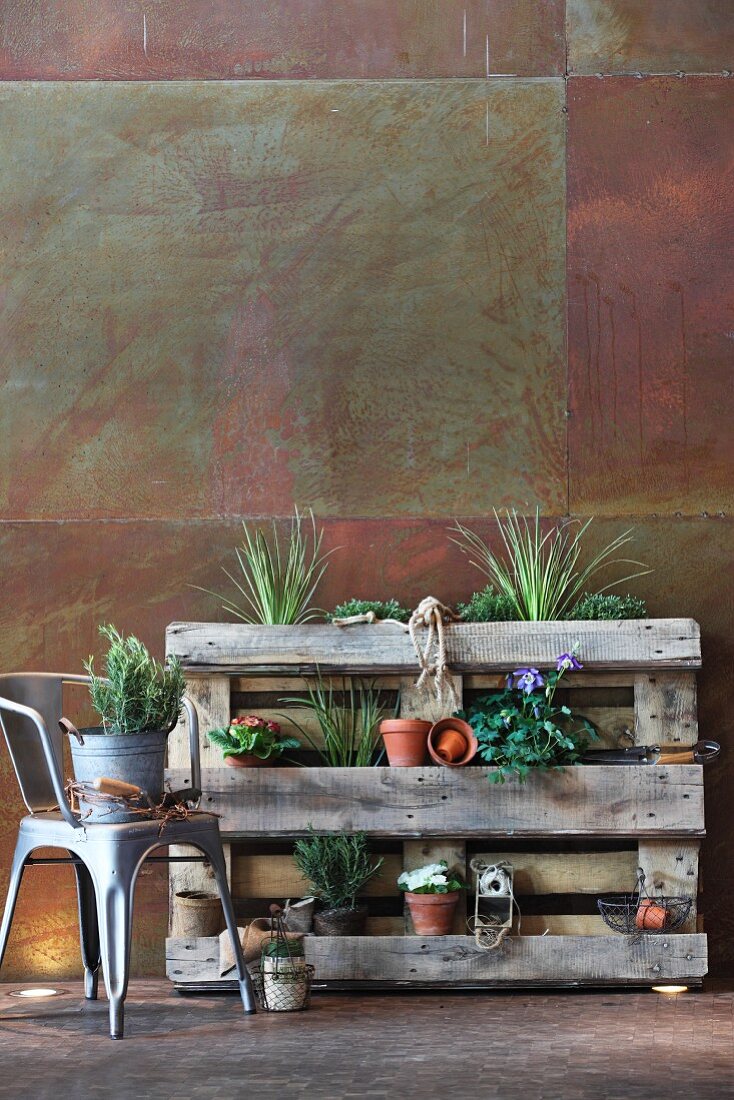 Pflanzregal aus Holzpalette an Cortenstahl Wand und Metallstuhl