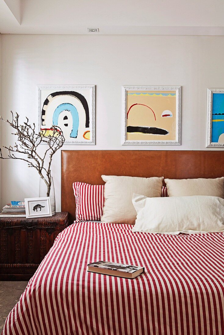 Red and white striped bedspread on double bed with headboard upholstered in brown leather below framed pictures on wall