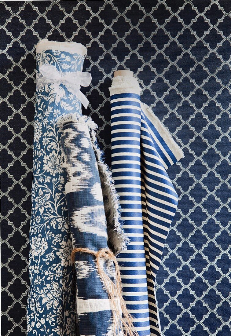 Bolts of fabrics in various patterns of blue and white against wallpaper with pattern of blue and white lozenges