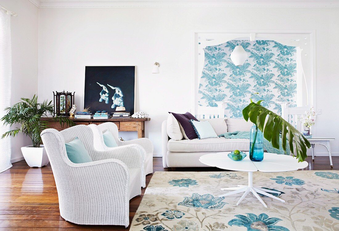 White wicker armchairs and sofa around white table in living room with turquoise patterns on Florence Broadhurst wallpaper and rug