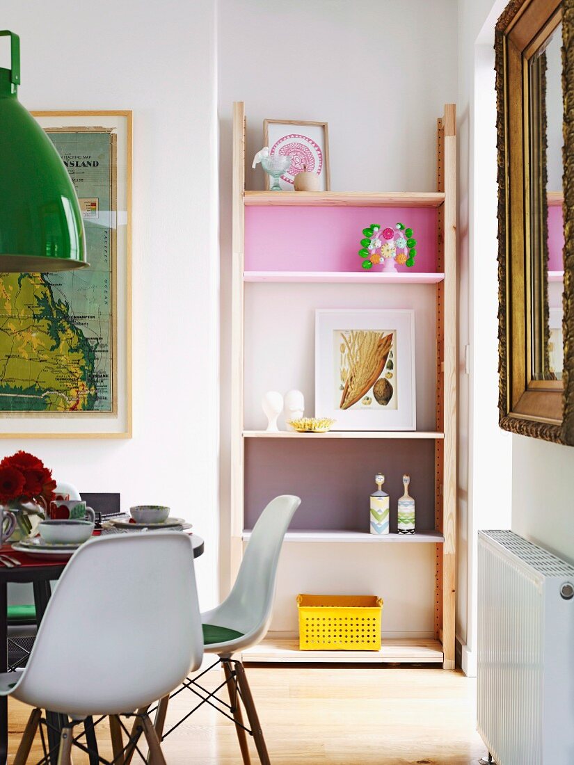 Shelving with compartment back walls in various colours in niche next to dining area with classic chairs and framed map