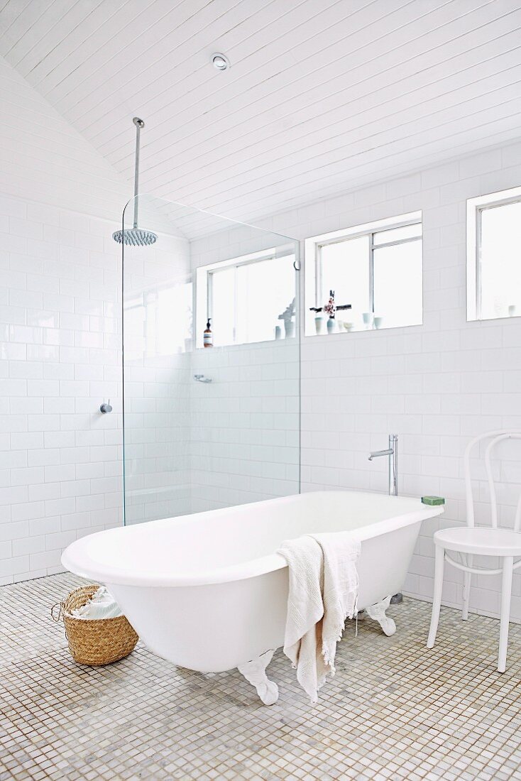 Freistehende Badewanne und weiss lackierter Thonetstuhl neben einer bodengleichen Regendusche mit Glasabtrennung