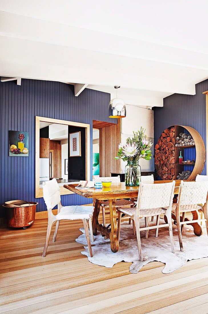 Essplatz mit Tierfell, rustikalem Tisch und Stühle aus Geflecht vor blau lackierter Holzwand