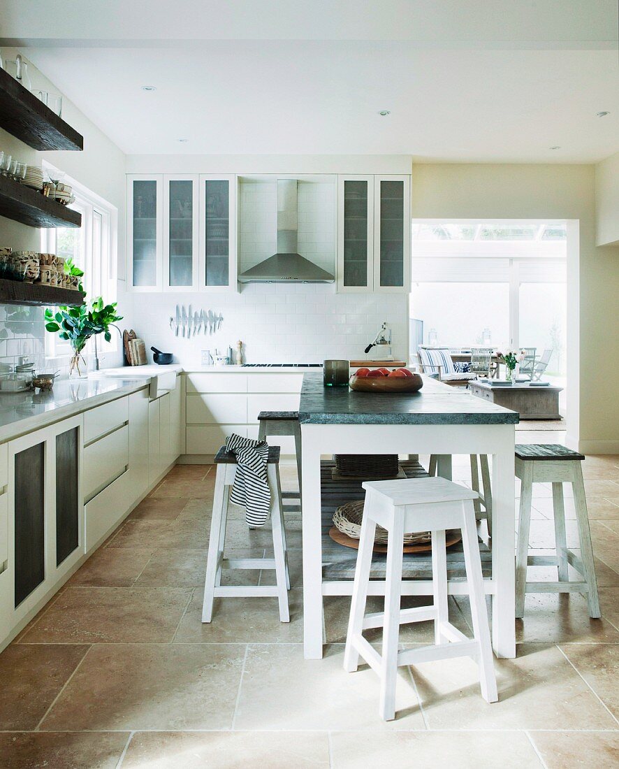 Island counter and stools in modern, white fitted kitchen with tiled floor