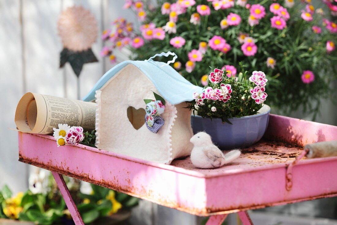 Selbstgebasteltes Vogelhaus aus weissen und himmelblauen Filz auf rostigem, pinkfarbenem Tabletttisch