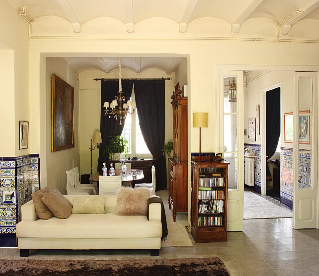 Herrschaftlicher Wohnraum mit Sofa in klassischem Stil vor offenem Essbereich und Blick durch offene Flügeltür in die Küche