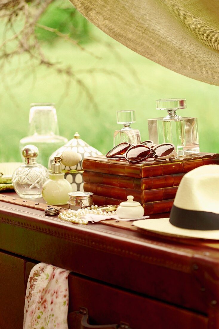 Bottles of perfume and sunglasses on hat on antique chest of drawers