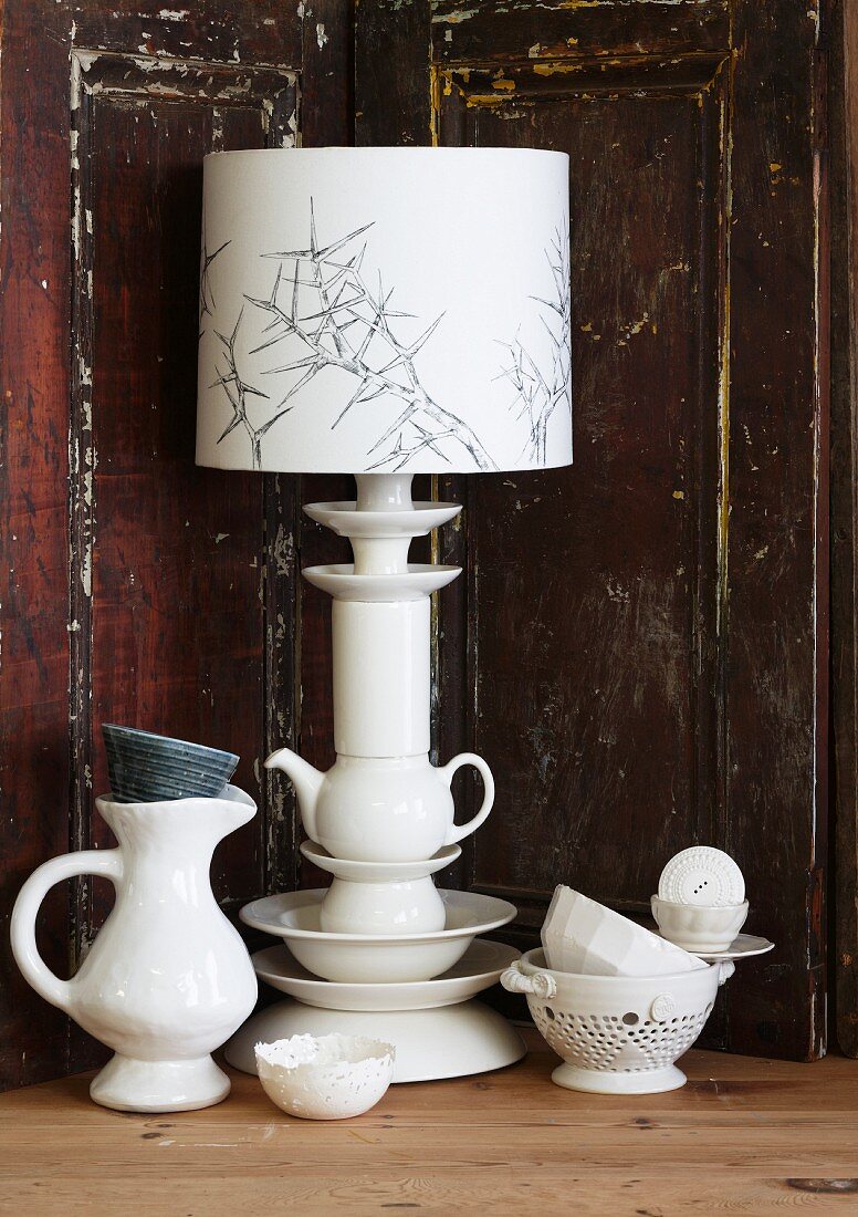 Tischlampe mit originellem Fuss aus gestapeltem Porzellangeschirr vor einer Holzrückwand mit abblätternder Farbe