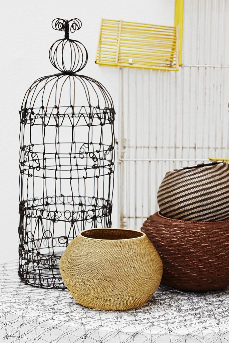 Old, ornate bird cage and various round baskets with wire rack in background