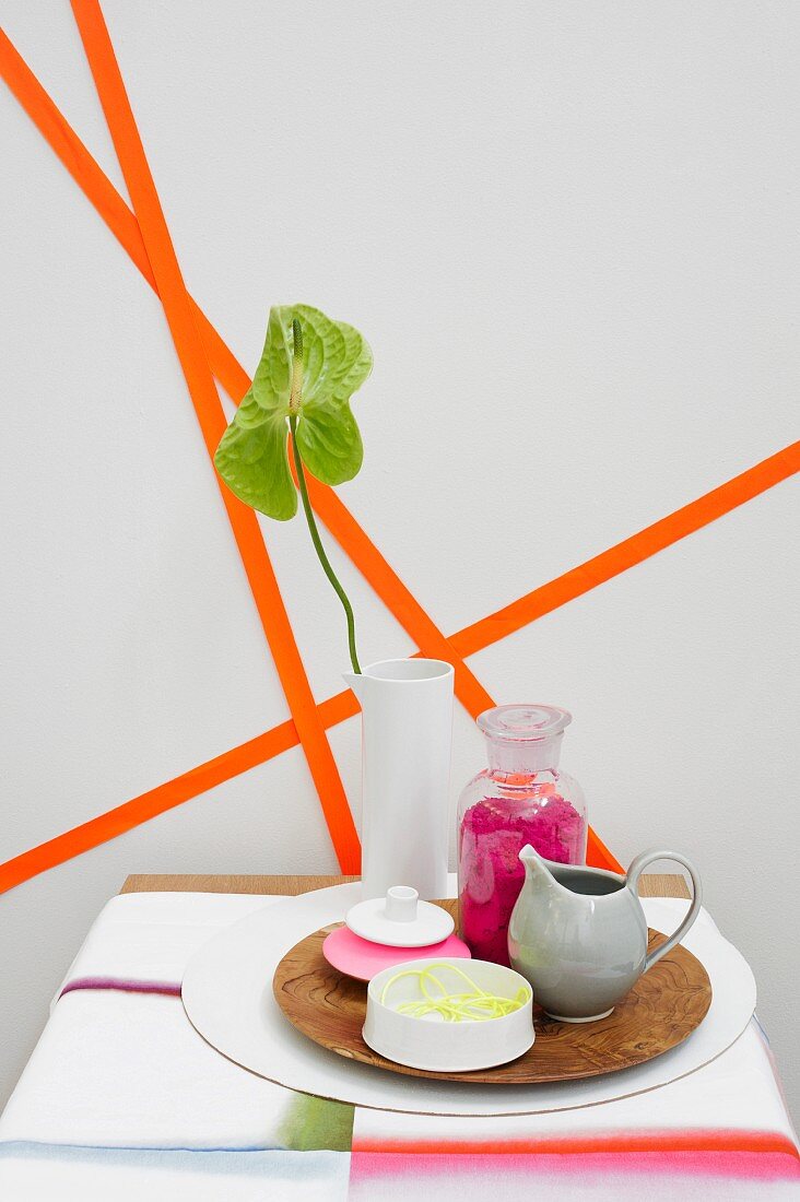 Containers on plate in front of geometric pattern of orange paper strips on wall