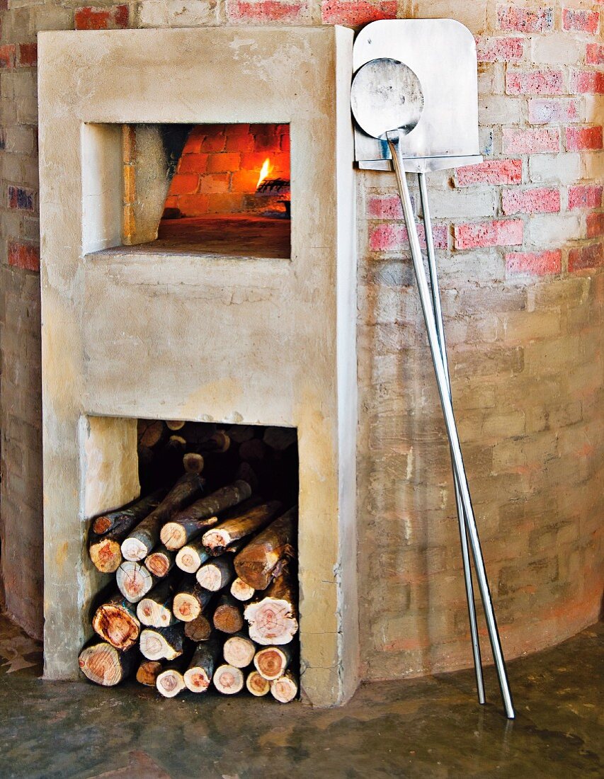 Masonry pizza oven with plastered log pile and oven surround; pizza peels leaning on wall to one side