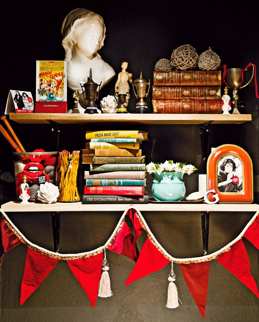 Stacked books, trophies and china bust of woman on simple shelves decorated with red bunting
