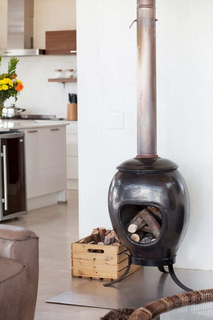 Ceramic stove filled with wood on stainless steel panel in open-plan interior