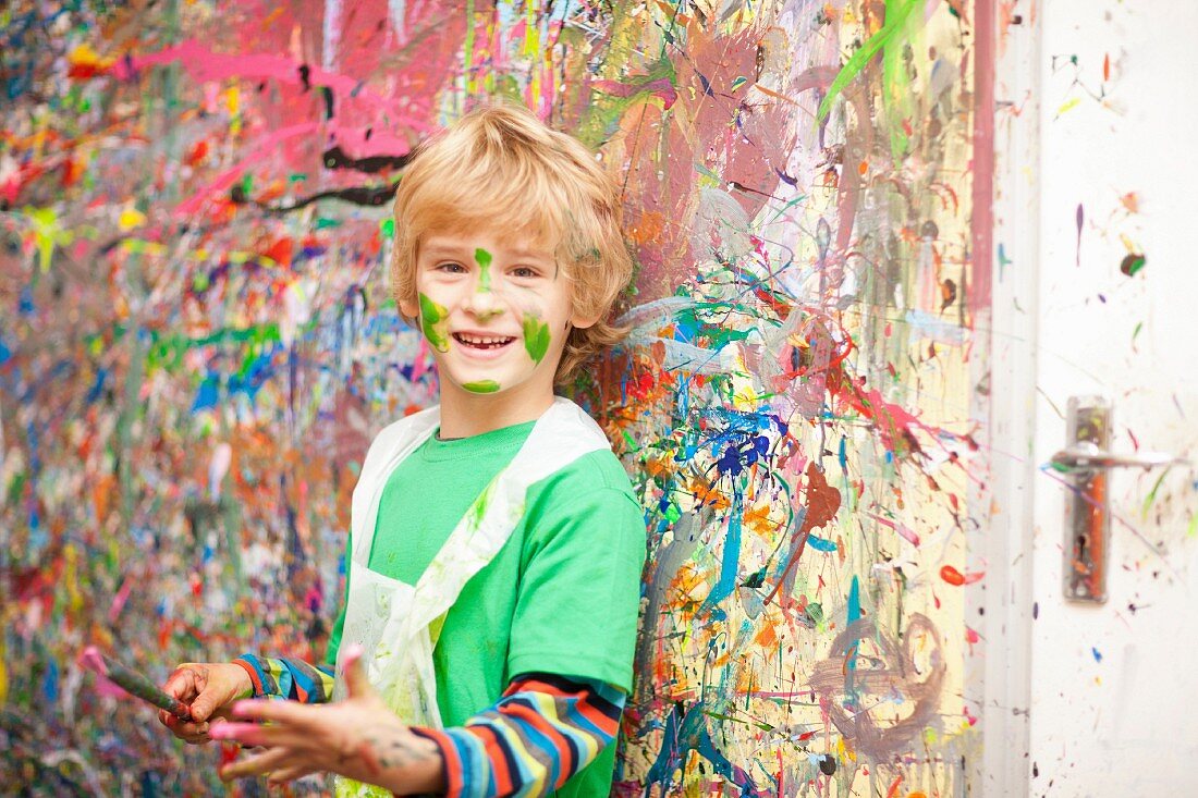 Junge mit Pinsel vor farbverschmiert Wand