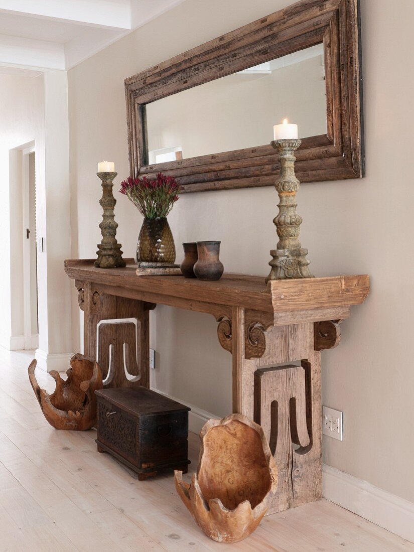 Bowl-like, wooden objets d'art and trunk on floor below candlesticks on rustic antique console table and framed mirror on wall