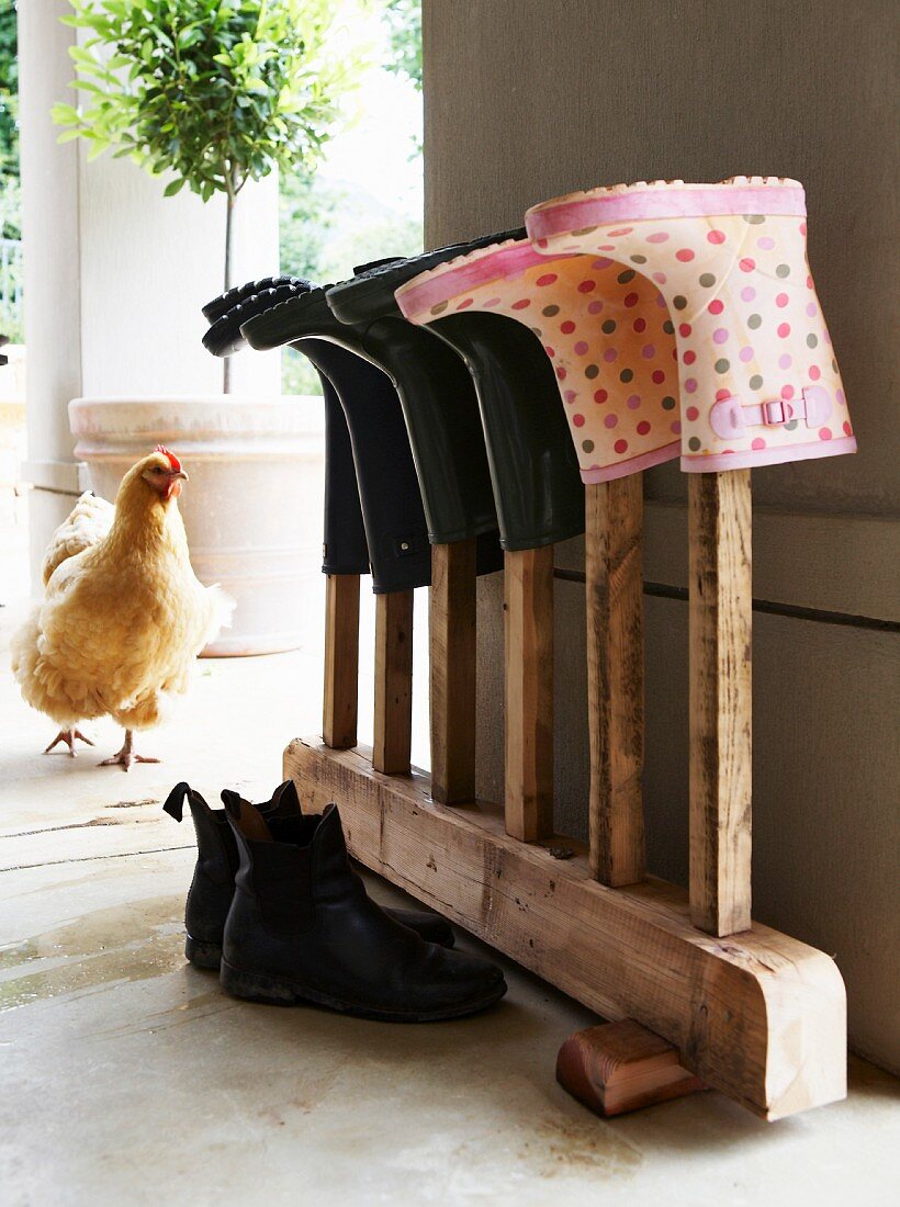 Gummistifel auf Vintage Holzständer, im Hintergrund ein Huhn auf Veranda