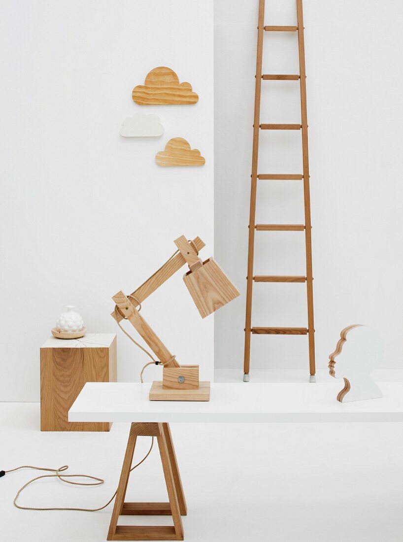 Holzobjekte in weißem Raum - Tischlampe aus Holz Bauteilen auf weisser Tischplatte mit Böcken vor Wand mit Deko-Objekten und Vintage Leiter