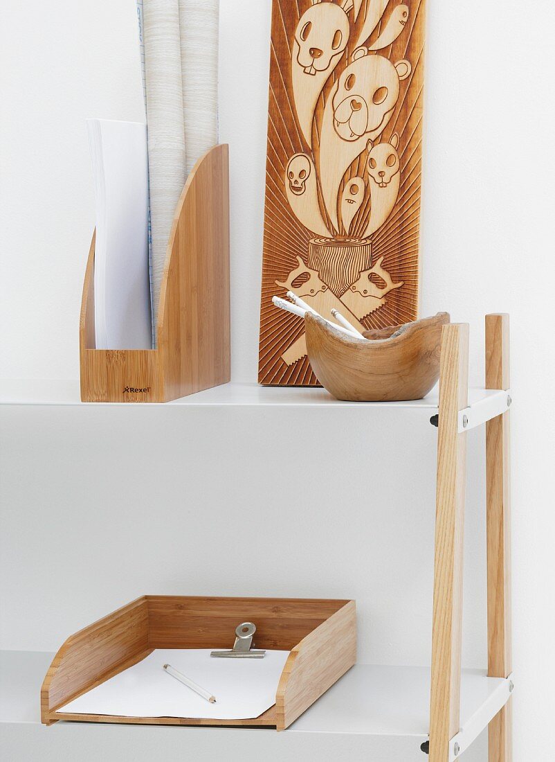 Wooden objects in white surroundings - half-height shelving with white metal shelves and wooden office furnishings next to wooden panel carved with animal motifs