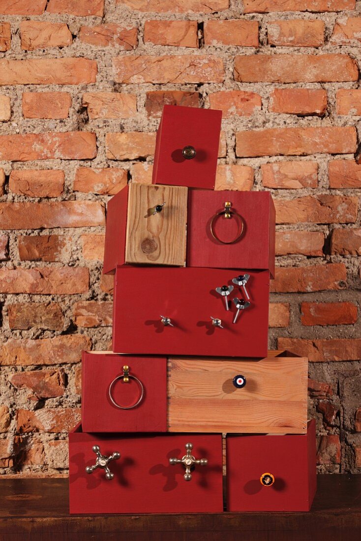 Gestapelte Kisten mit teilweise rotbraunen Fronten und angeschraubten Bauteilen vor rustikaler Ziegelwand
