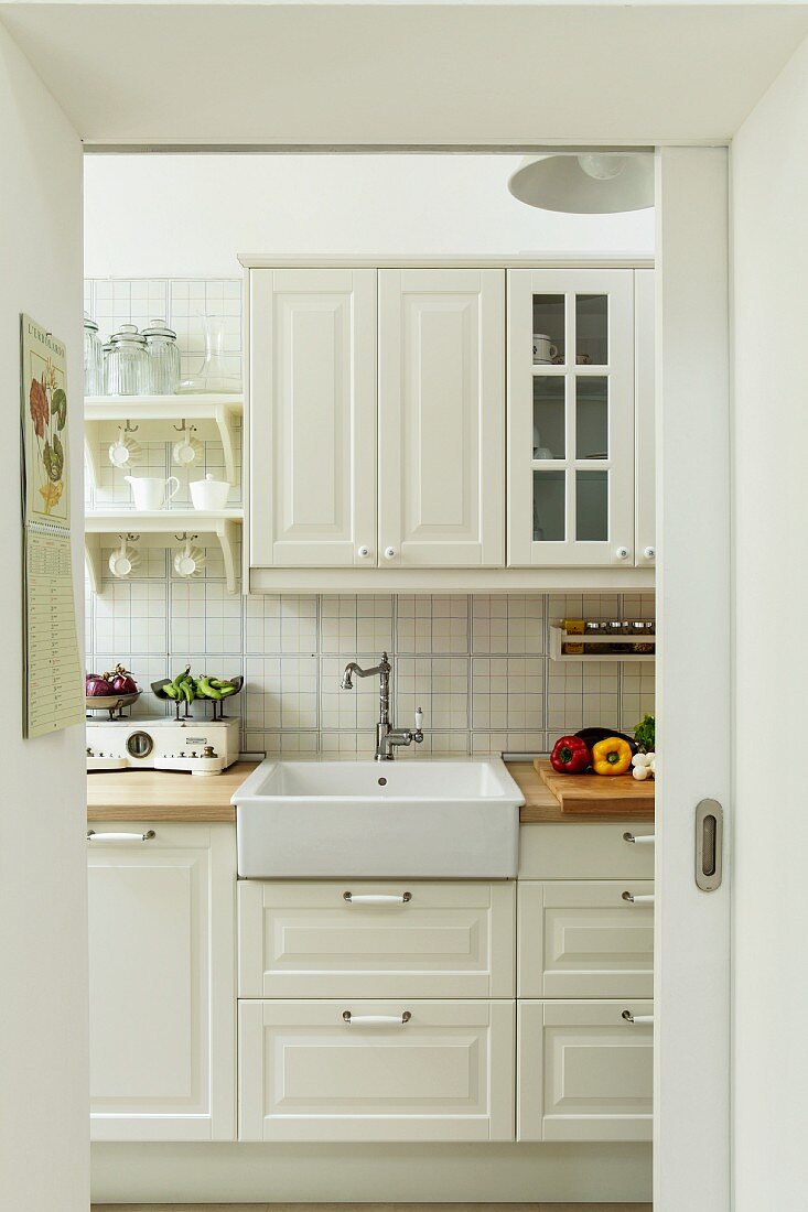 Blick durch offene Schiebetür auf helle Küche im Landhausstil, Vintage Küchenarmatur an Spülbecken