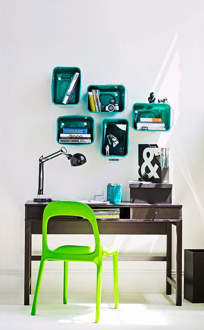 Schreibplatz mit Schreibtisch und grellgrünem Stuhl, an der Wand aufgehängte Kunststoffboxen zur Aufbewahrung