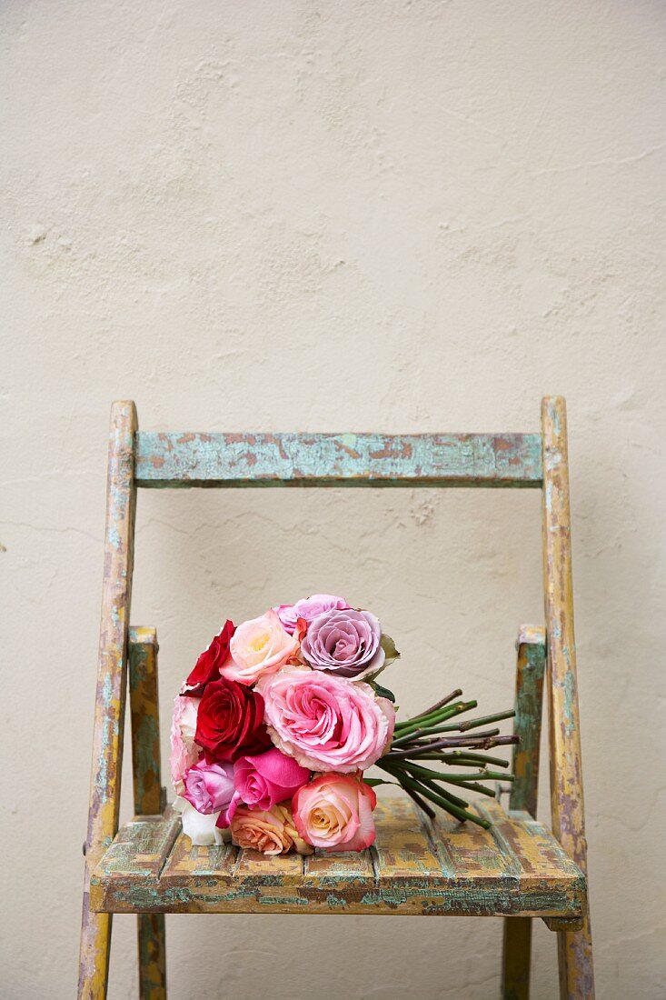 Bouquet of roses of different colours on weathered wooden chair