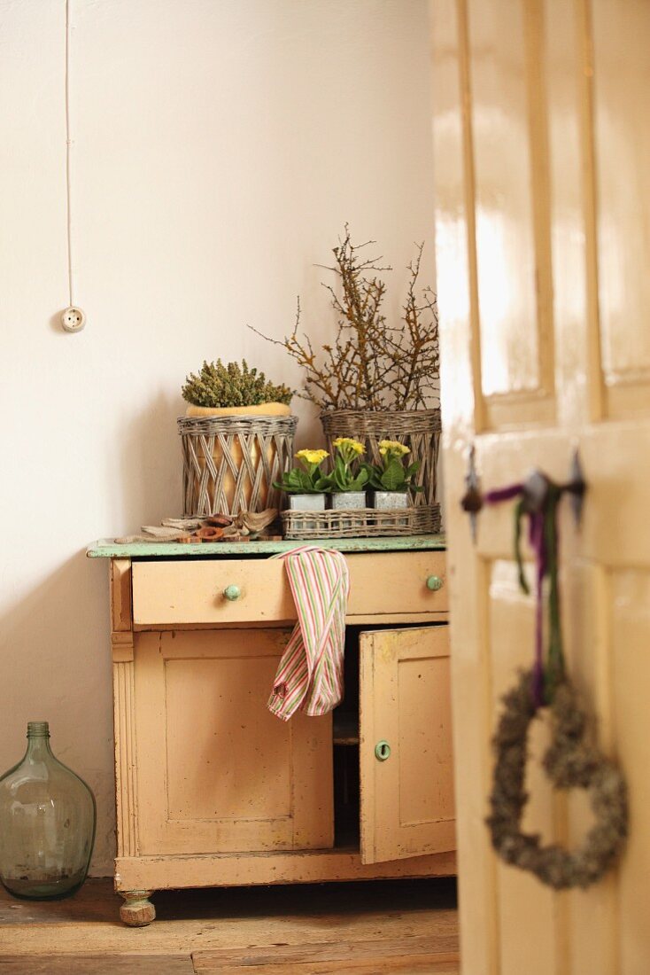 View through open door of rustic cabinet with potted flowers and baskets of twigs