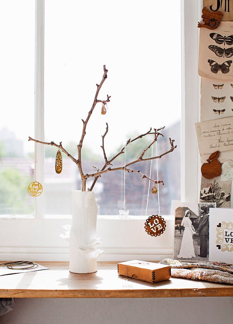 Zweig mit Schmuck behängt in weißer Vase auf Fensterbrett