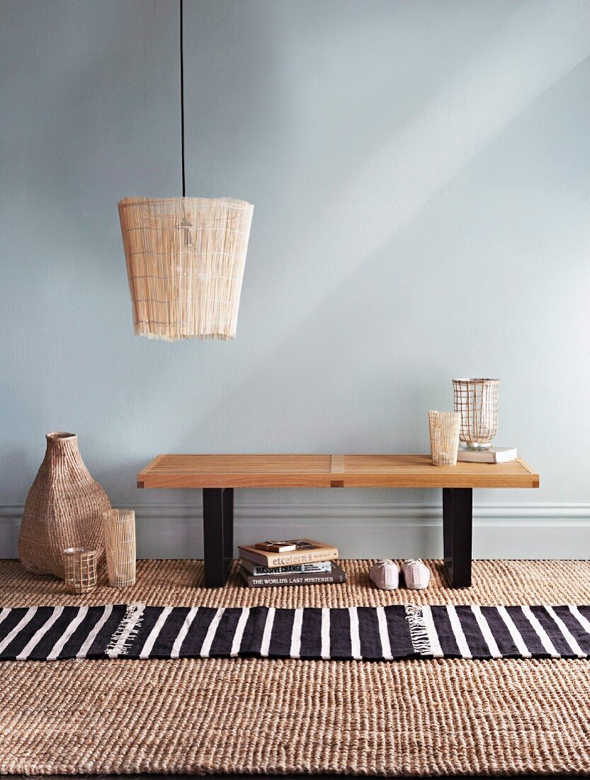 Hand-crafted lampshade made from bamboo place mat above small wooden table against blank wall; sisal carpet and striped rug on floor