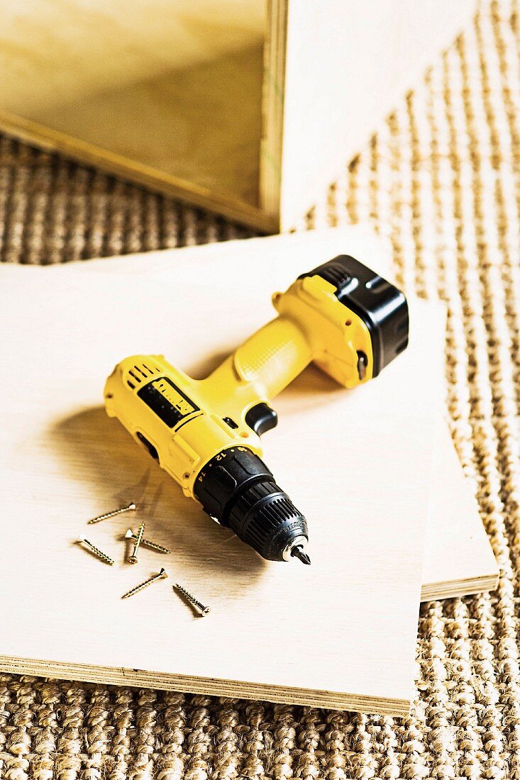 Yellow cordless drill-driver lying on cut plywood panel