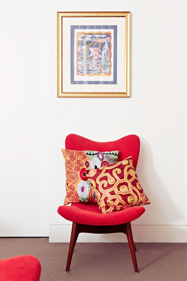 Kissen auf rotem gepolsterten Retro-Stuhl vor Wand mit gerahmtem Bild