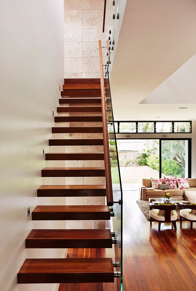 Moderne Treppe mit Massivholzstufen in offenem Wohnraum mit Loungebereich vor Terrassenfenster
