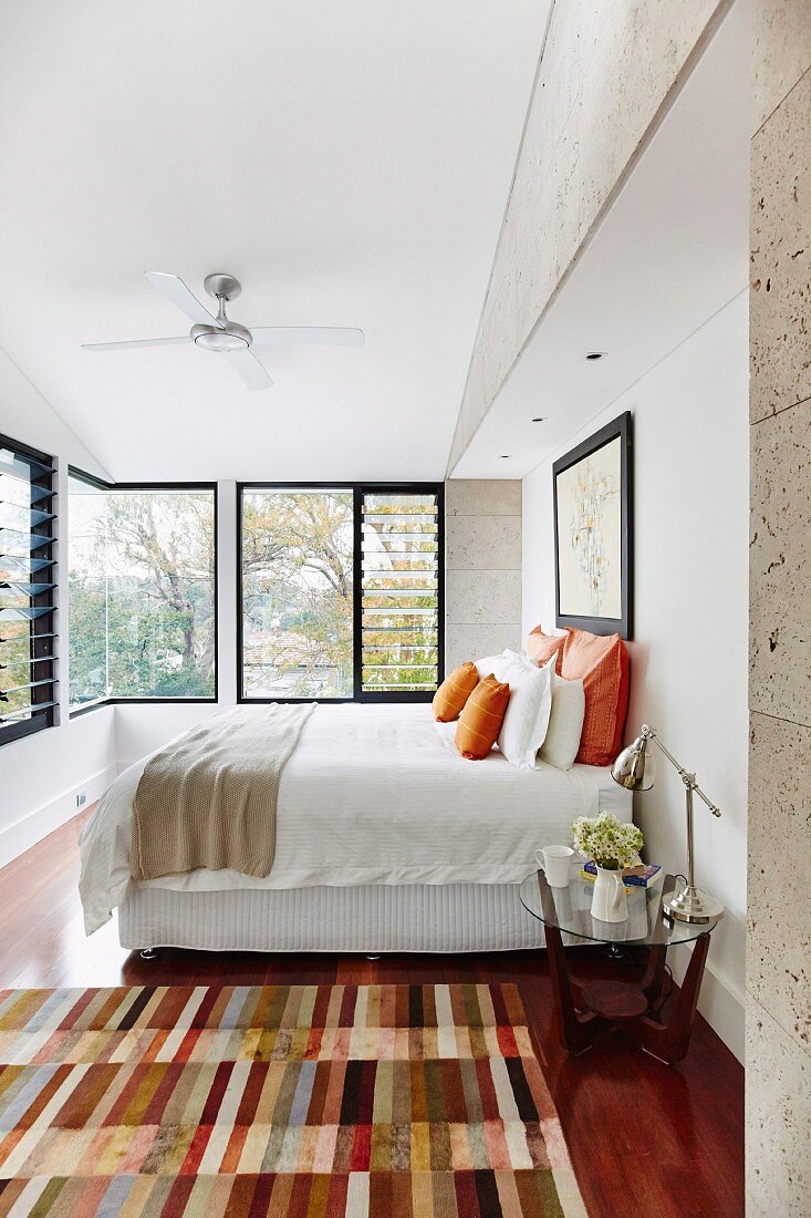 Patchwork rug in front of double bed in contemporary bedroom with row of windows