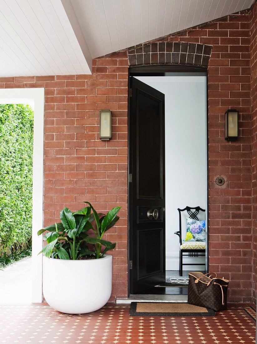 Überdachter Eingangsbereich in Klinkerfassade mit Durchgang zum Garten; geöffnete Eingangstür gewährt Einblick ins Haus