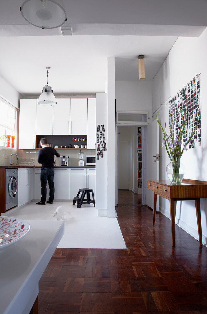 Open-plan interior with white fitted kitchen and hall area with mosaic parquet flooring and 50s console table