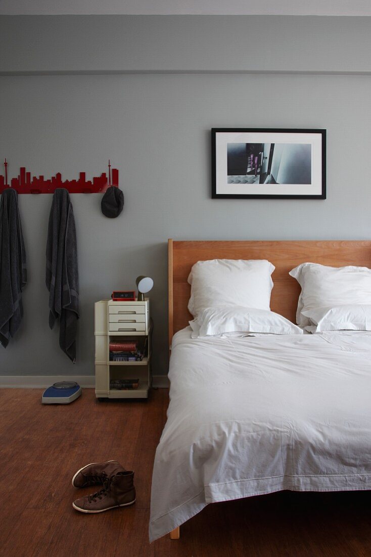 Fotokunst über massgefertigtem Bett mit Kopfteil aus Holz in grau getöntem Schlafraum; seitlich rote Garderobenleiste