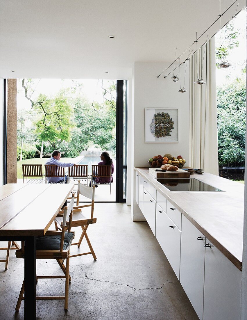 Offene Küche mit weisser Küchenzeile als Raumteiler und Terrassenzugang