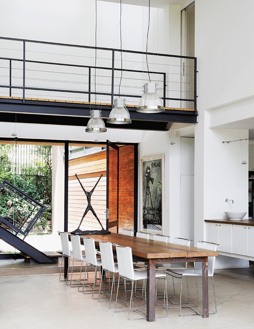 Open-plan interior with bridge in upper storey above dining area in front of partially visible staircase and glass wall leading to terrace