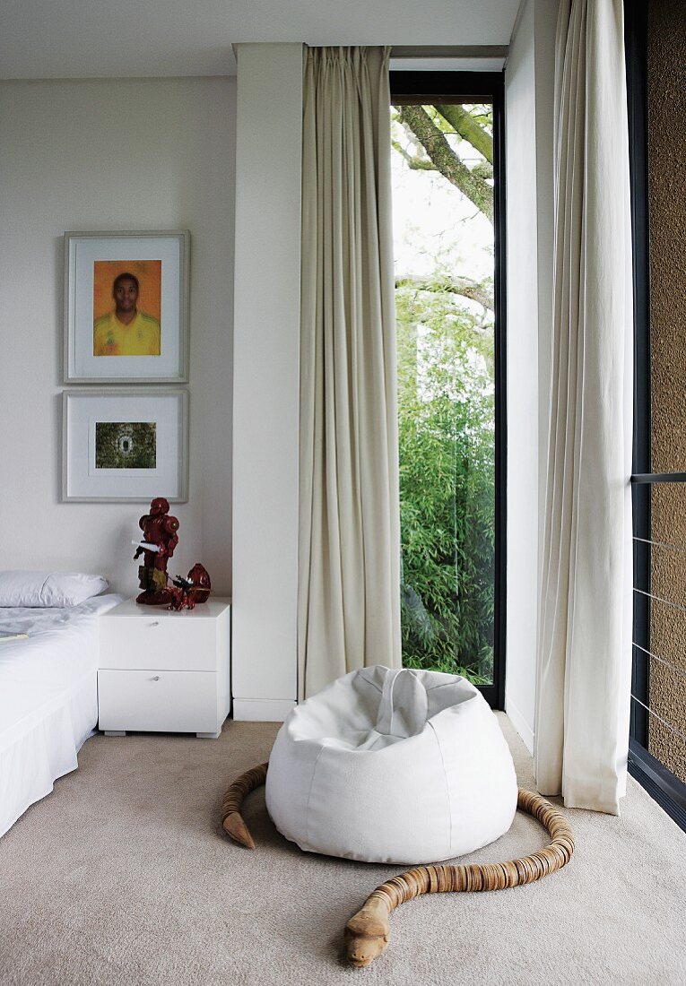Schlange aus Holzteilen um weissen Sitzsack vor raumhohem Fenster mit weißem Vorhang in modernem Schlafzimmer
