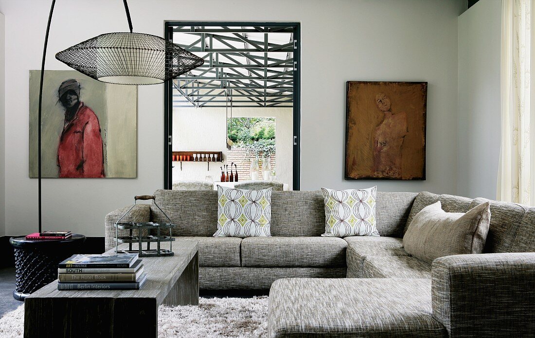 Gemütliche Sofalandschaft in Grau und minimalistischer Couchtisch unter lässiger Bogenlampe mit Geflecht-Schirm in moderner Wohnraumecke