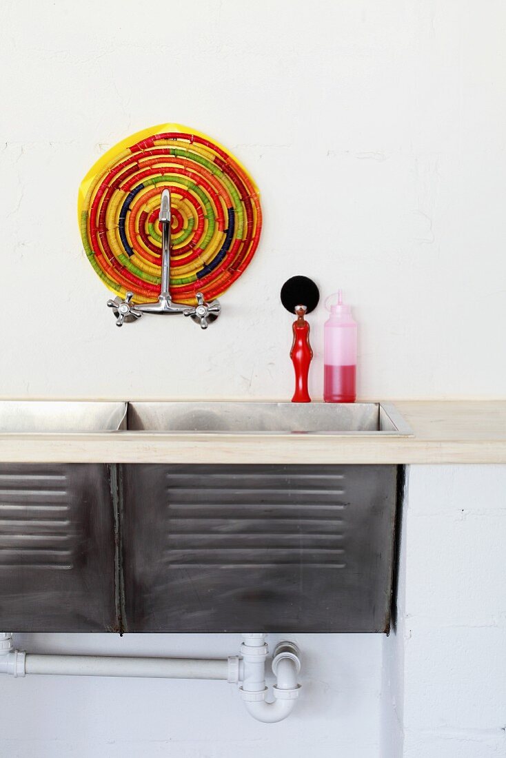 Simple sink with two basins and colourful trivet mat behind wall-mounted tap fitting