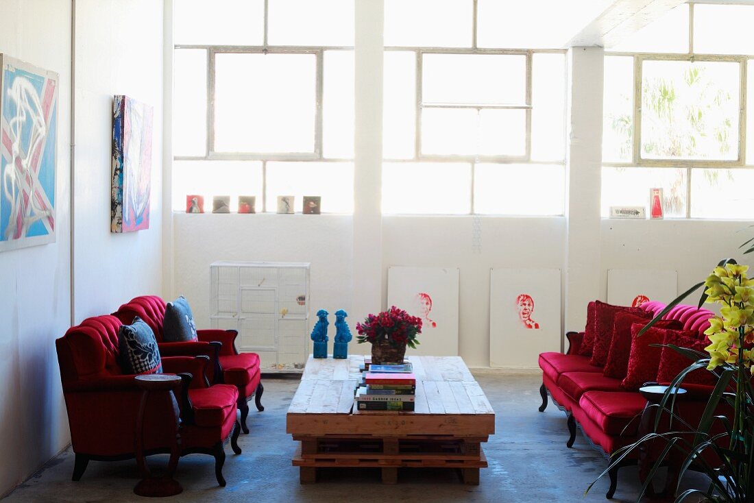 Antike Sessel mit rotem Samtbezug um rustikalen Palettentisch in loftartigem Wohnraum mit Fensterband