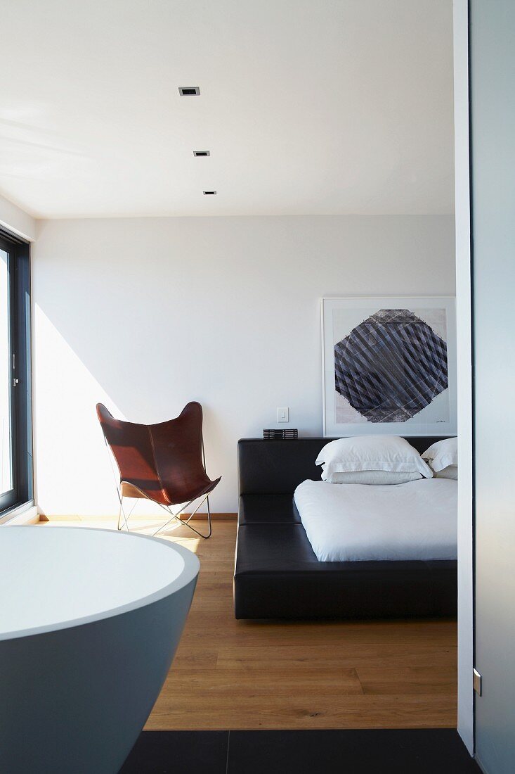 Blick von Bad Ensuite auf schwarzes Doppelbett mit weißer Bettwäsche und braunem Designer Butterfly Chair