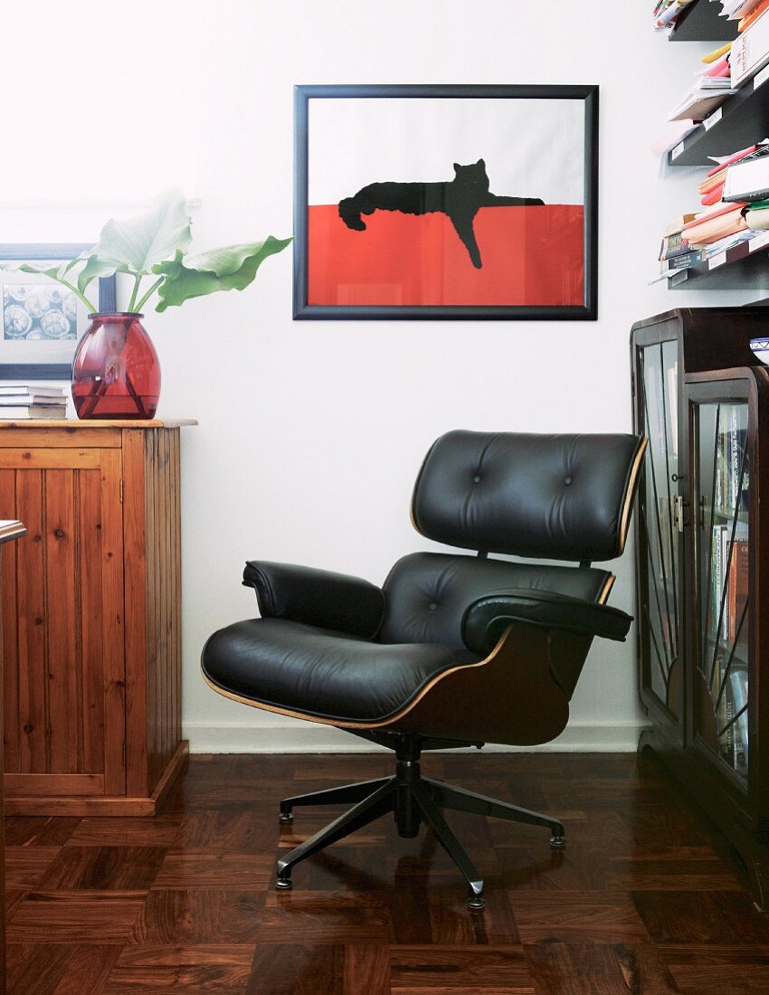 Lounge chair with black leather cover in corner in front of framed picture of cat