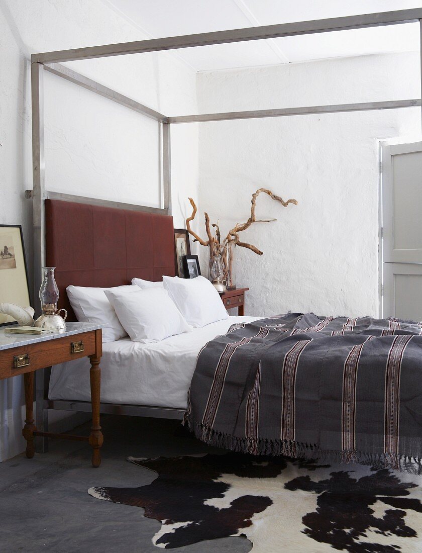 Schlichtes Schlafzimmer mit Himmelbett, auf Bett gestreiftes Tagesdecke, im Vordergrund Tierfell auf Boden