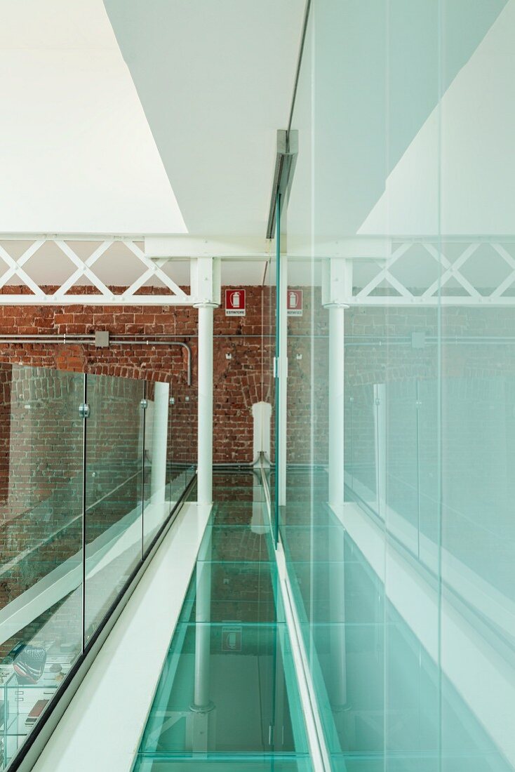 Loftgalerie mit Boden und Brüstung aus Glas, am Ende eine Stahlträgerkonstruktion vor Backsteinwand und seitliche Begrenzung durch Glasfront