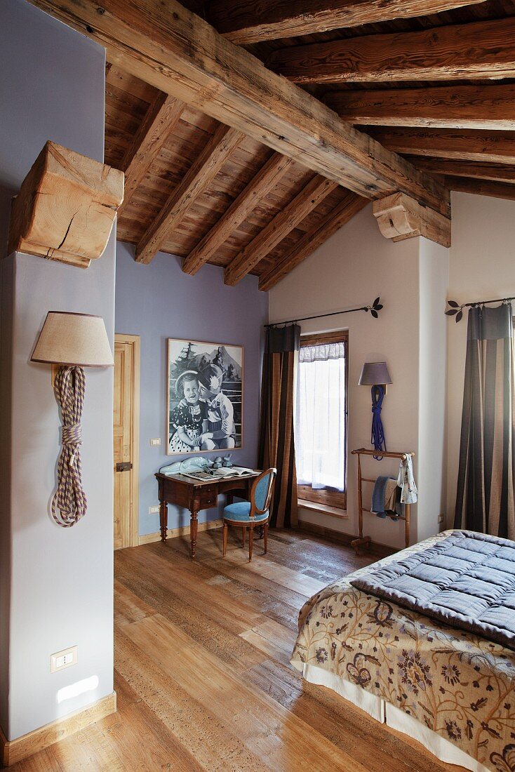 Schlafzimmer unter dem Dach mit rustikaler Holzbalkendecke und teilweise violett getönten Wänden