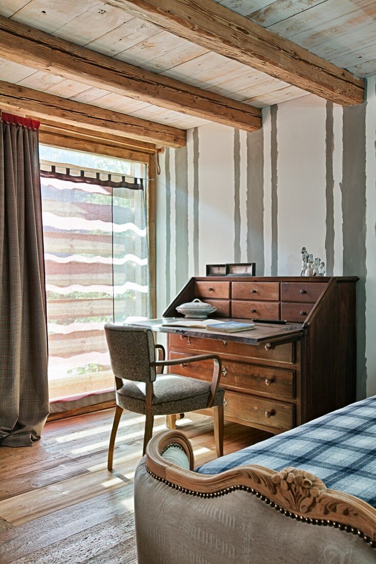 Teilweise sichtbares Bett mit antikem Gestell und Stuhl vor Sekretär in rustikalem Schlafzimmer